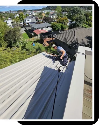 Technician in safety harness on a roof cleaning out a gutter, restoring it's ability to drain water.