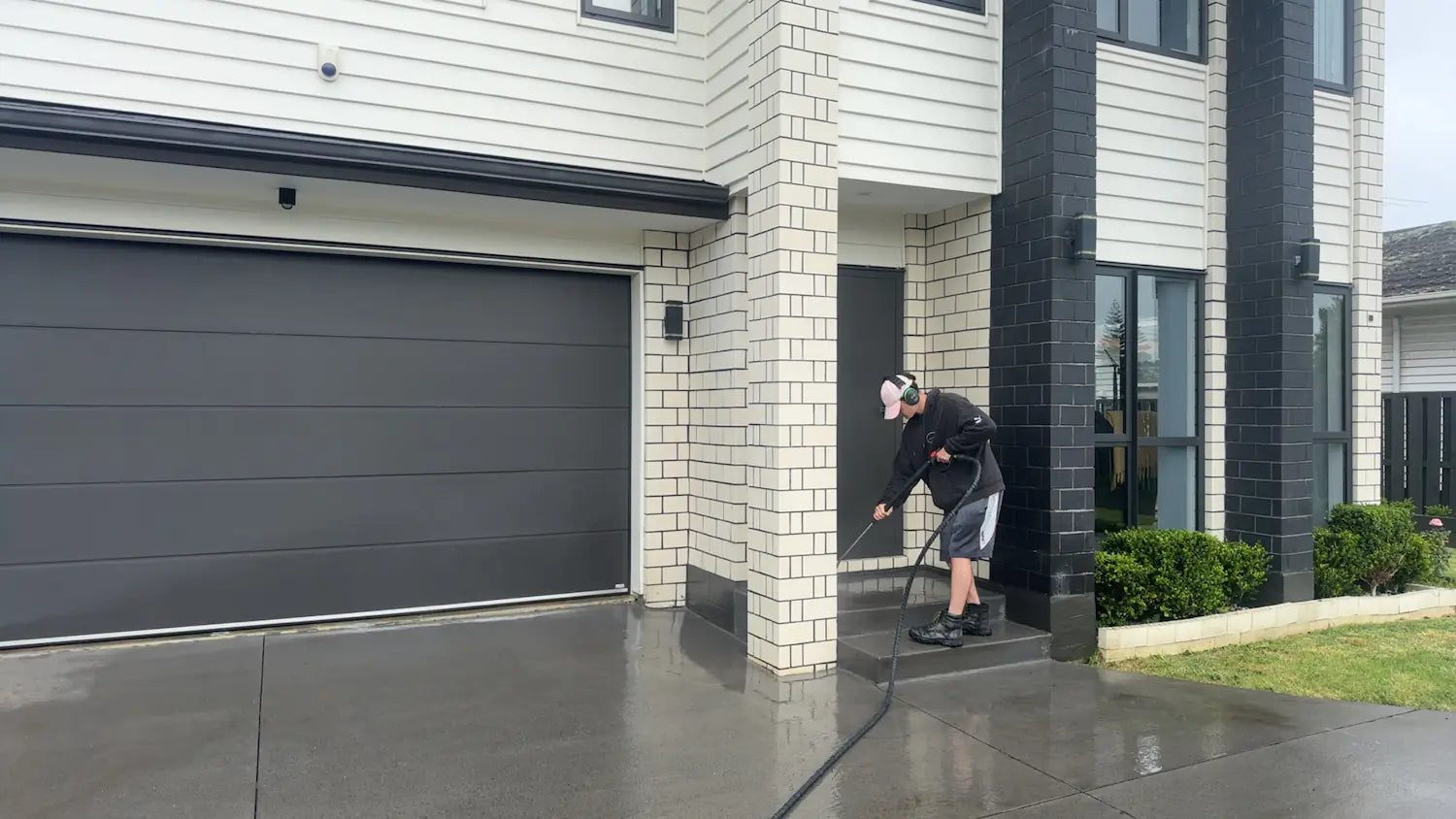 Pressure washing a modern house exterior with driveway, shown in action by a technician wearing safety gear.