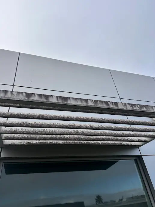 Close-up of a building's aluminium louvre and cladding streaked with grime before exterior signage cleaning.